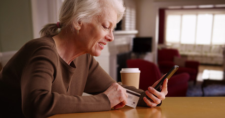 Modern senior woman shopping online through her phone sitting inside home