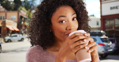 Cheerful African woman drinking coffee and looking at camera in town street