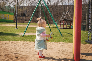 Little baby girl walking near the swings.