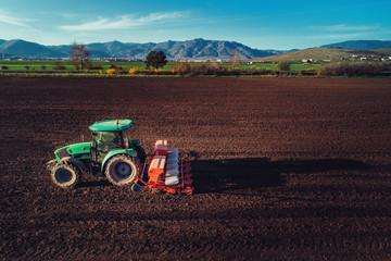 Farmer with tractor seeding crops at field
