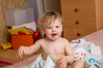 Funny baby after bathing sits on the bed in a towel with a hood.