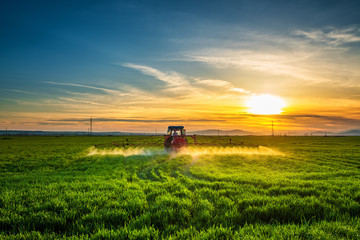 Naklejka premium Farming tractor plowing and spraying on field