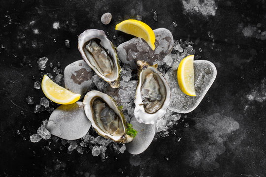 Opened oysters, dry ice and lemon on a black stone table. Top view.