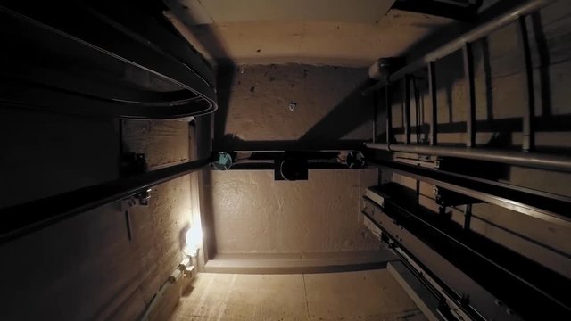 The cabin moves up in an elevator shaft. The view is directed downwards. The camera is moving. The lights in the shaft give the ride its own rhythm.