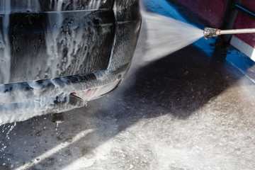Jet of wash with soap water high pressure is sent to the rear lights of the machine. Driver, girl wahsing her car in the stall of a car wash, using a high pressure water jet.