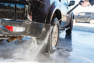 Washing jet with soap water high pressure is directed to the wheel of the car. Driver, girl wahsing her car in the stall of a car wash, using a high pressure water jet. Washing car with water splash