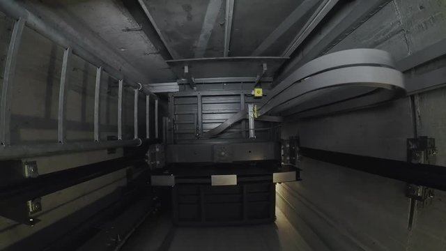 In an illuminated elevator shaft, the cabin moves up. The ride goes through the 5 floors of the house.