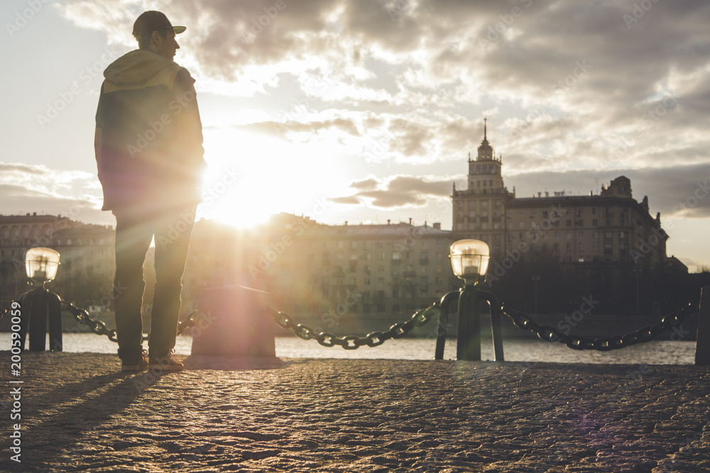 Wall mural young man in snapback and jacket standing near the river in the city