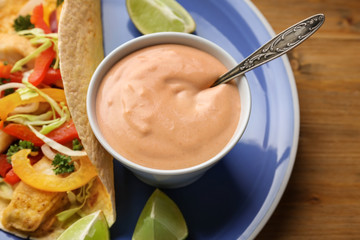 Plate with tasty creamy sauce in bowl and fish taco on wooden table