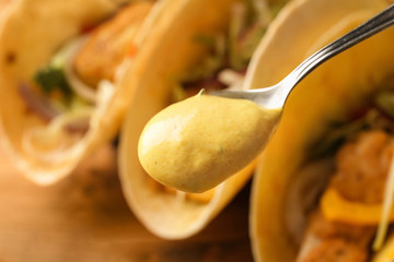 Spoon with tasty creamy sauce for fish taco on blurred background