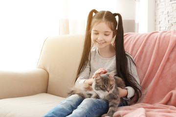 Cute little girl with cat sitting on sofa at home