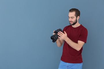 Young photographer with professional camera on color background