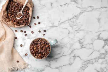 Ceramic cup and paper bag with coffee beans on marble background, top view