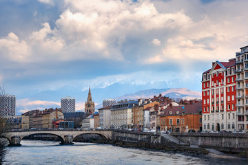 Scenic view of the banks of the Isere river and bridge, Collegiate Church of Saint-Andre with French Alps on the background, Grenoble, France