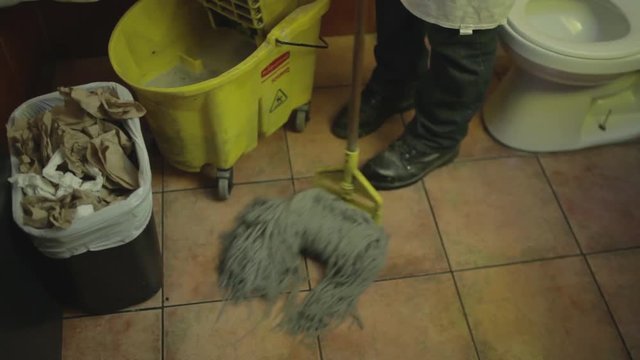 Man cleaning the floor with mop in a restroom