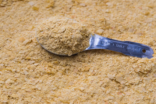 Full frame close-up vegan nutritional yeast with stainless steel tablespoon