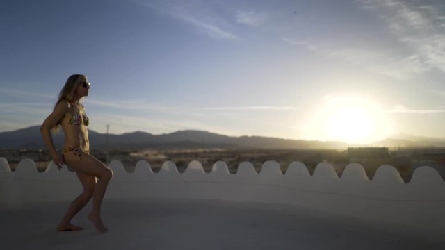 Exotic belly dancer practices a body wave against a blue sky and setting sun.