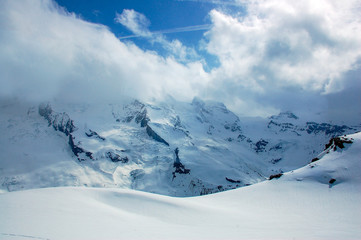 Fototapeta na wymiar High mountains under snow with clouds and blue skies in Switzerland 