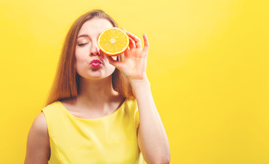 Happy young woman holding a half orange on a yellow background