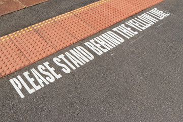 Please Stand Behind The Yellow Line warning in stencilled white paint