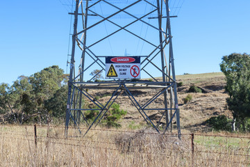 a red, black and white Danger, Do Not Climb warning sign on an electricity transmission tower in rural Australia