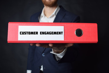 A businessman holds a folder with the inscription:CUSTOMER ENGAGEMENT