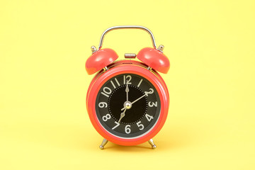 Red vintage alarm clock on yellow background.