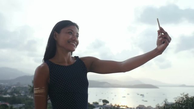 Smiling asian woman making selfie photo on mobile phone. Happy woman using smart phone for mobile selfie. Posing and smiling asian woman portrait