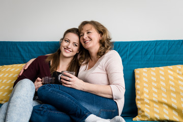 Affectionate mother and daughter sitting on sofa at home