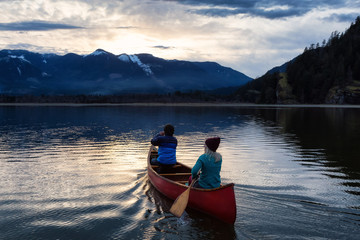 Adventurous people on a wooden canoe are enjoying the beautiful Canadian Mountain Landscape during a vibrant sunset. Taken in Harrison River, East of Vancouver, British Columbia, Canada.