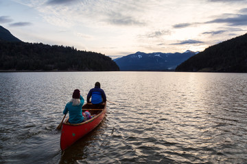 Fototapeta na wymiar Adventurous people on a wooden canoe are enjoying the beautiful Canadian Mountain Landscape during a vibrant sunset. Taken in Harrison River, East of Vancouver, British Columbia, Canada.