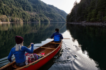 Couple friends canoeing on a wooden canoe during a sunny day. Taken in Harrison River, East of Vancouver, British Columbia, Canada.