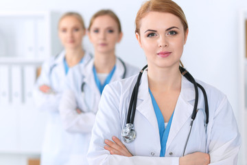 Fototapeta premium Beautiful female medical doctor standing at hospital in front of medical group. Physician is ready to help patients. Medicine and health care concept
