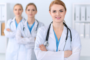 Fototapeta premium Beautiful female medical doctor standing at hospital in front of medical group. Physician is ready to help patients. Medicine and health care concept