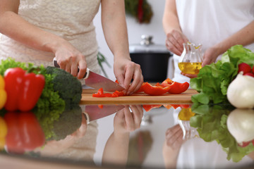 Closeup of human hands cooking in kitchen. Mother and daughter or two female cutting bell pepper for fresh salad. Healthy meal, vegetarian food and lifestyle concepts
