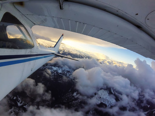 Fototapeta premium Small airplane flying over the Canadian Mountain Landscape during a vibrant sunset. Taken near Squamish, North of Vancouver, British Columbia, Canada.