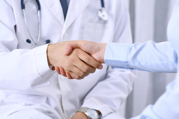 Obraz na płótnie Canvas Male doctor and woman patient shaking hands. Partnership in medicine, trust and medical ethics concept