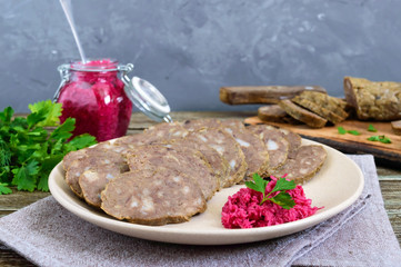 Home made dietary sausage from the liver on a wooden table. Sausage cut into pieces on a plate with horseradish sauce.