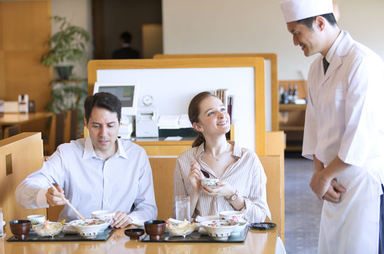 板前と話しながら日本料理を食べる外国人の男女