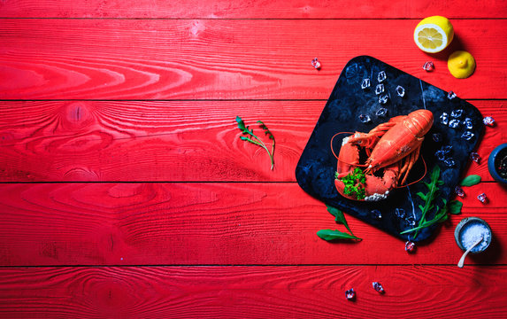 Red lobster with a bouquet of parsley in a clove, small white snails grown on the lobsters shell, on a black stone tray on red wooden background, Copy space
