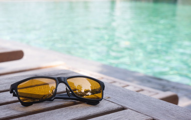 Fototapeta na wymiar sunglassed on wood table near swimming pool