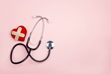 Stethoscope and heart with adhesive plaster on pink background. Flat lay and copy space.