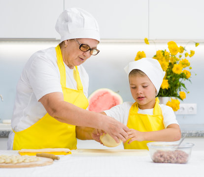 grandmother teaches the child to knead the dough in the kitchen
