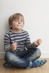 Niño (5 años) sentado en el suelo meditando con los ojos cerrados y boca cerrada.