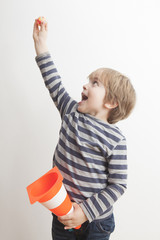 Niño (5 años) contento sujetando un cono de tráfico y mirando hacia arriba sujetando con su otra mano una pequeña pelota.