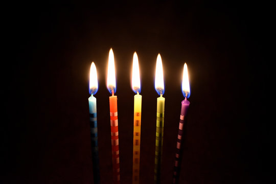 Cake candles on a dark background stock images. Colored cake candles. Burning cake candles. Birthday background images. Party candles on a black background