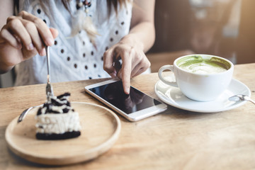 Young woman using smart phone and eating cake