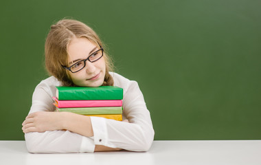 Happy teen girl with books on the background of a school board looking away. Space for text