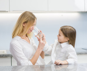 Obraz na płótnie Canvas Mom and daughter drink water in the kitchen
