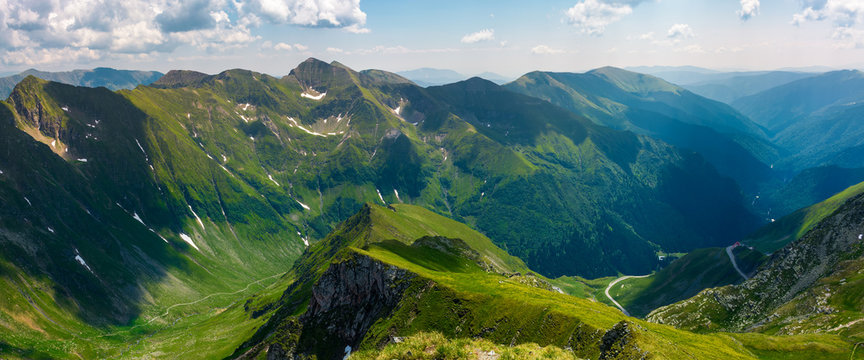 panorama of Fagarasan mountain ridge in summertime. lovely landscape with cliffs and grassy hills over the valley. TransFagarasan road in the left corner runs through the valley in to the distance